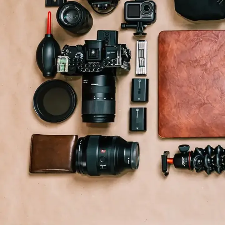 Overhead flat lay of a creator's kit: camera body, lenses, an action camera, spare batteries and a flexible tripod
