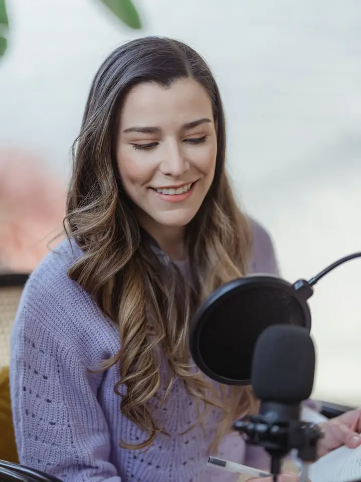 Creator writing notes in a planner while recording at a microphone