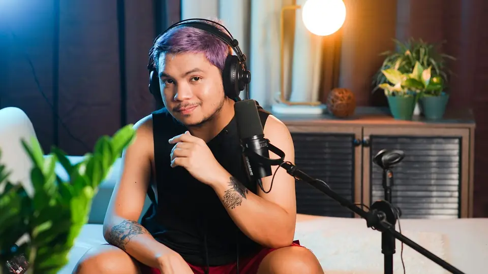 Podcaster in headphones at a condenser microphone in a warmly lit home studio