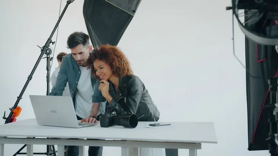 Two photographers reviewing shots on a laptop in a studio ringed with softboxes
